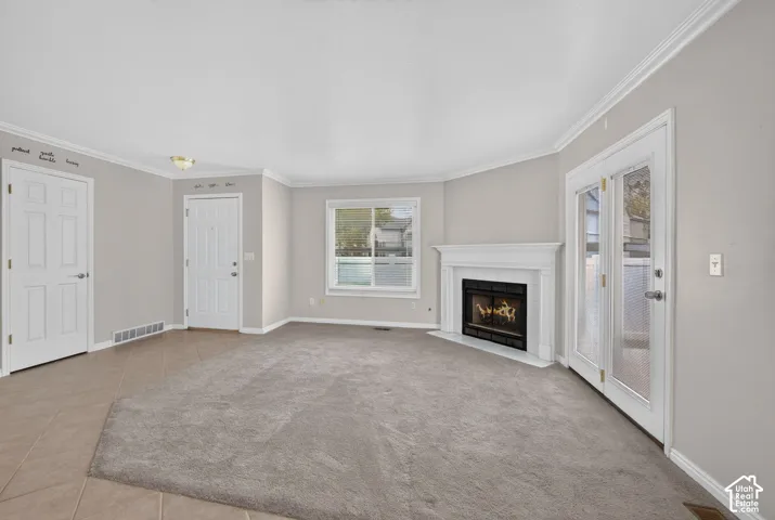Neutral-toned room featuring a central fireplace with a white mantel, glass-paneled double doors, neutral carpeting, and tiled entry flooring
