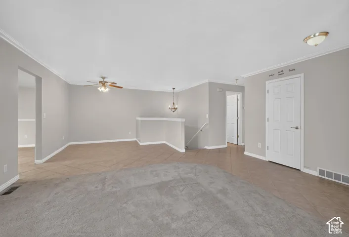 Neutral-toned interior featuring ceramic tile flooring, neutral wall-to-wall carpeting, a ceiling fan with integrated lighting, a multi-arm chandelier, and a six-panel interior door