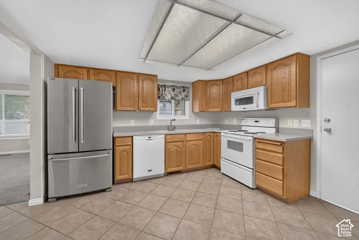 Kitchen featuring natural wood cabinetry, solid surface countertops, tile flooring, stainless steel French-door refrigerator, and white appliances