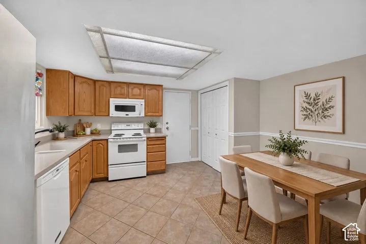 Kitchen featuring wood cabinetry, white appliances, tile flooring, recessed panel doors, and a flush-mount light fixture