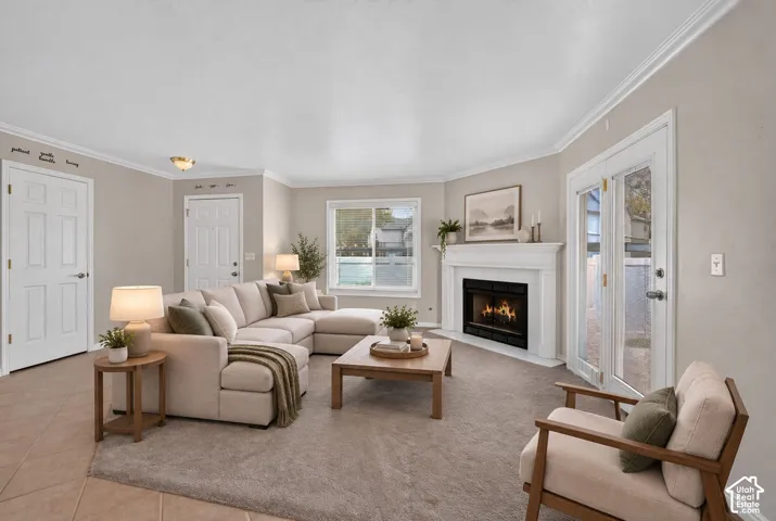 Living area featuring a white mantel fireplace, neutral carpeting, tile flooring, crown molding, and glass-paned double doors