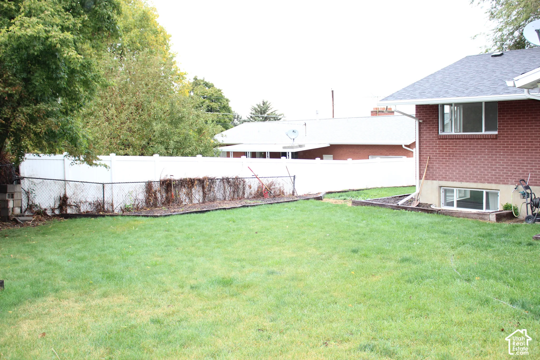 Backyard featuring a level lawn, white vinyl perimeter fencing, and terraced landscape edging