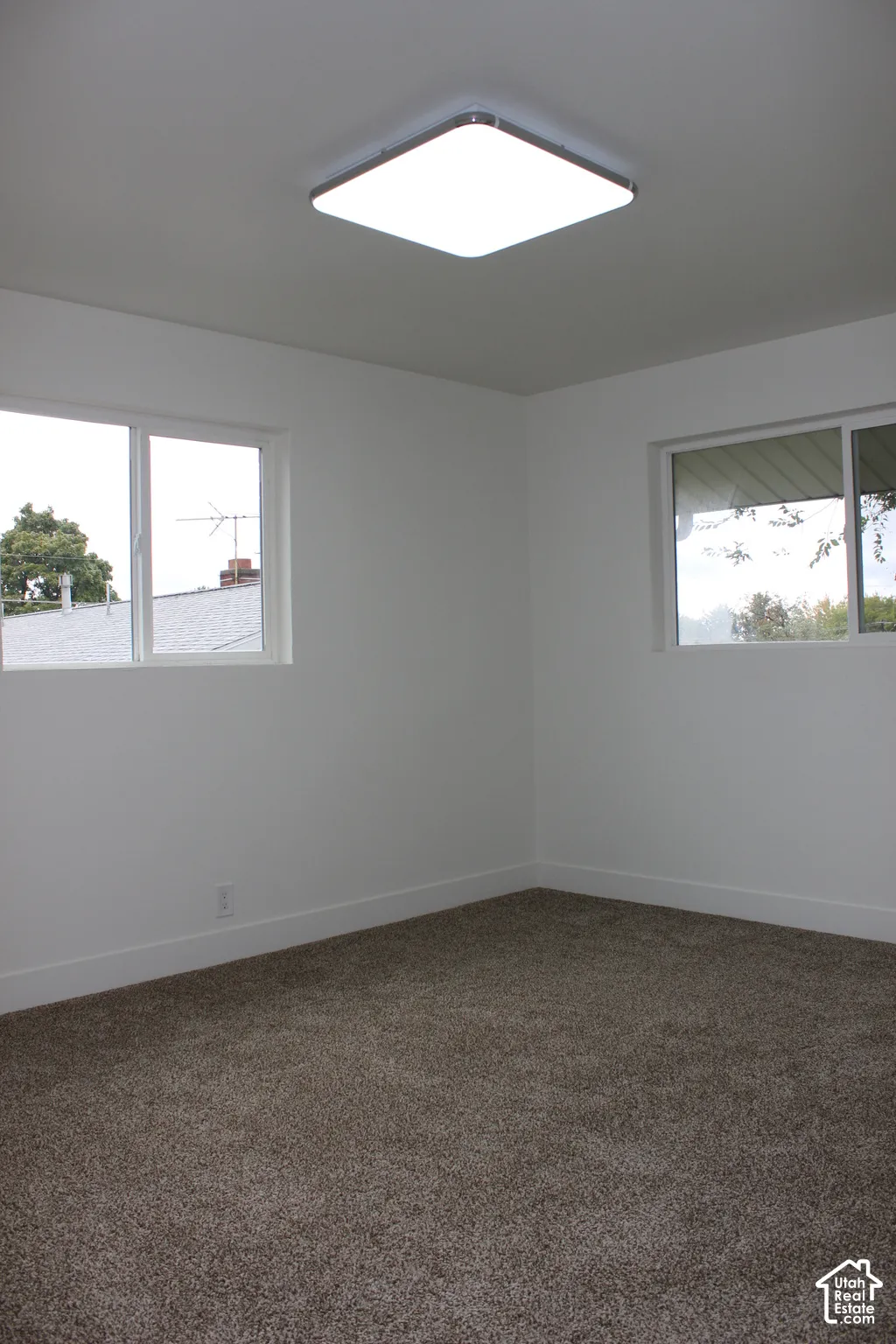 Interior space featuring neutral-toned carpeting, matte white walls, dual sliding-glass windows, and a flush-mount square ceiling light fixture