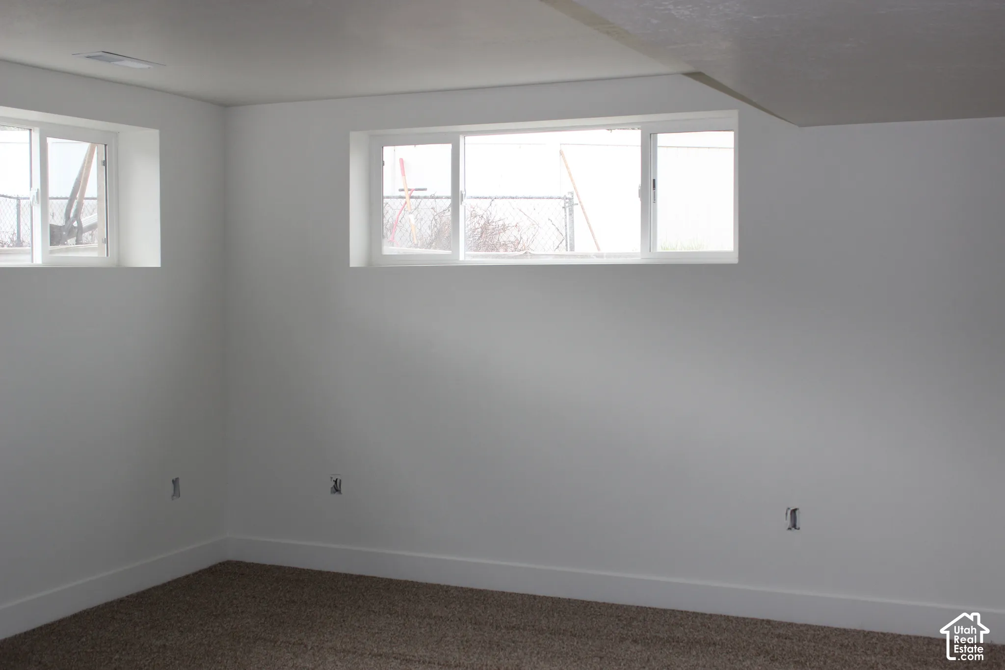 Neutral-toned interior space featuring white-painted walls, carpeted flooring, and white-framed sliding windows