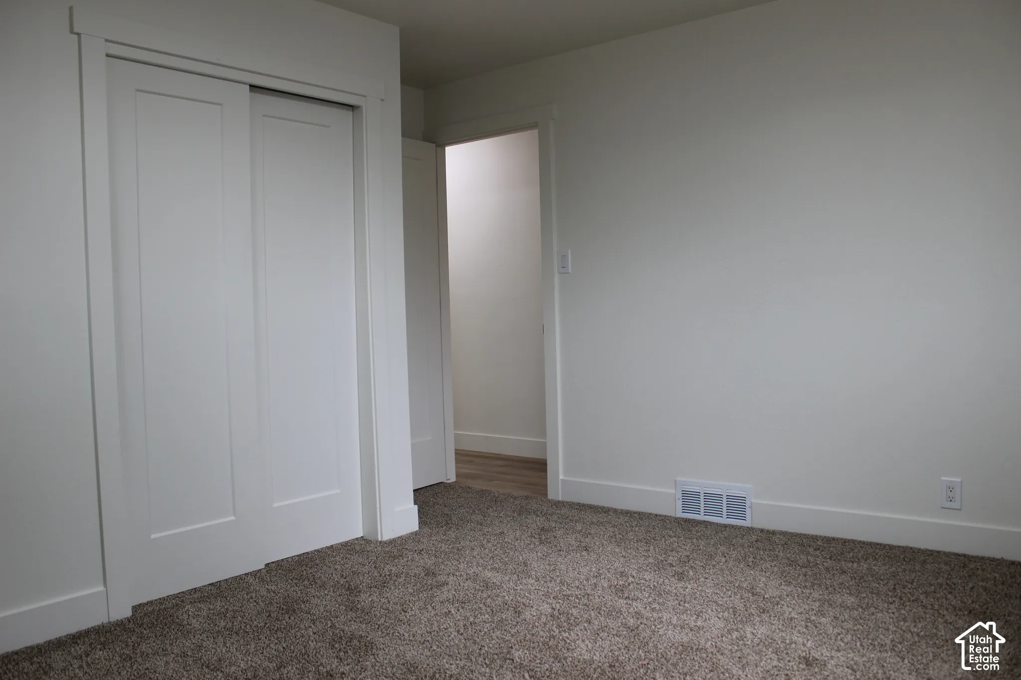 Neutral-toned carpeted flooring, white two-panel sliding closet doors, and interior trim with matching door casings