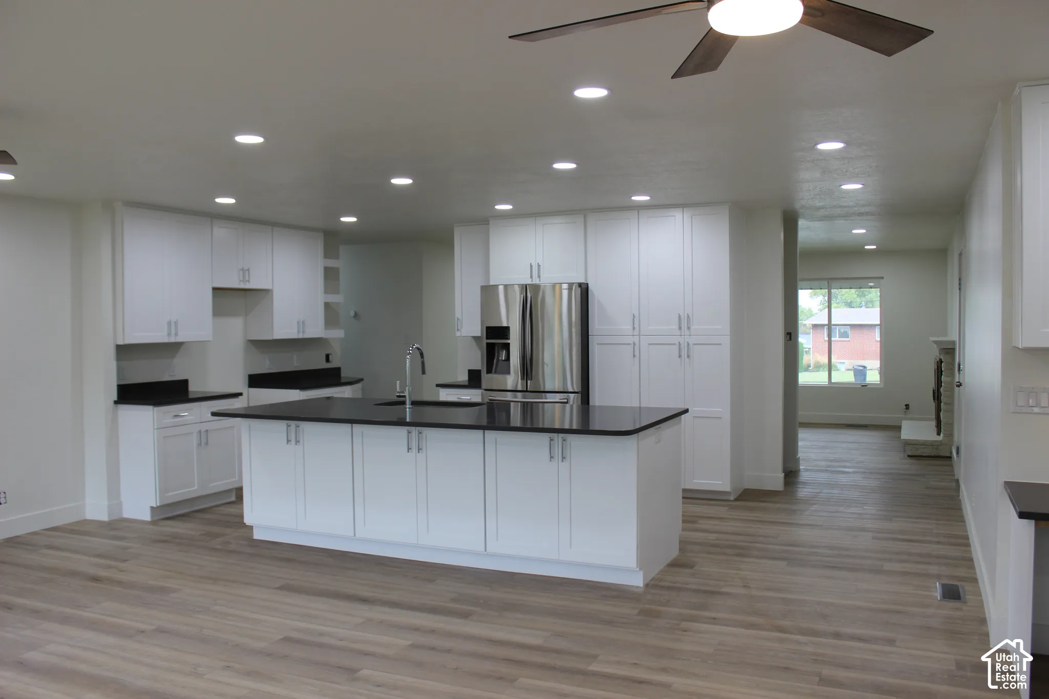 Kitchen featuring white cabinetry, dark stone countertops, a central island with an integrated sink, recessed lighting, and wood-finish flooring
