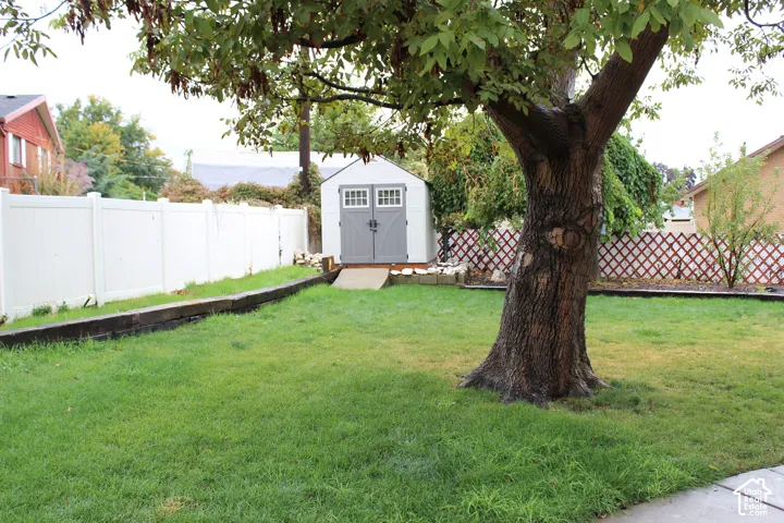 Fenced backyard featuring a lawn area, mature tree, timber retaining walls, and a detached storage shed