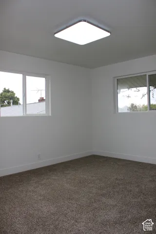 Interior space featuring neutral-toned carpeting, matte white walls, dual sliding-glass windows, and a flush-mount square ceiling light fixture