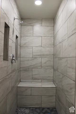Walk-in shower featuring large-format neutral tile walls, an integrated tiled bench, dual recessed wall niches, and a contrasting hexagonal tile floor with polished chrome fixtures
