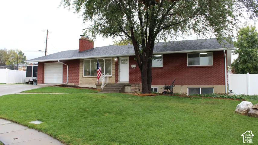 Rambler-style exterior featuring red brick masonry, a shingle roof, an attached garage, and a central chimney