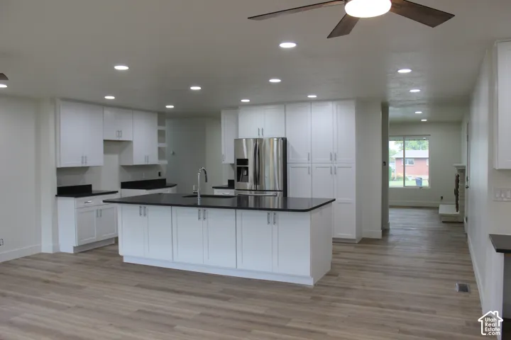 Kitchen featuring white cabinetry, dark stone countertops, a central island with an integrated sink, recessed lighting, and wood-finish flooring