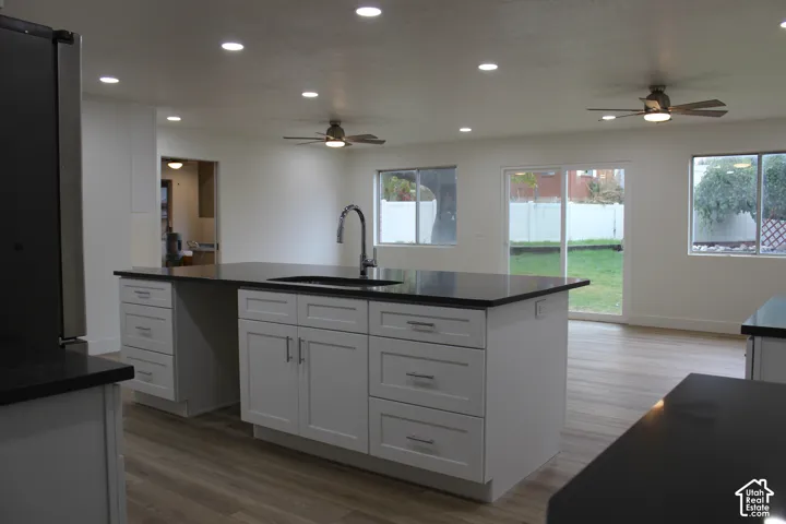 Kitchen island with white shaker-style cabinetry, dark countertops, and an integrated sink with a gooseneck faucet