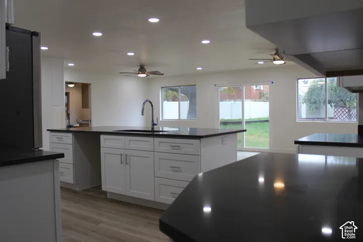 Kitchen featuring a central island with dark stone countertops, white shaker-style cabinetry, recessed ceiling lighting, wood-finish flooring, and a sliding glass door