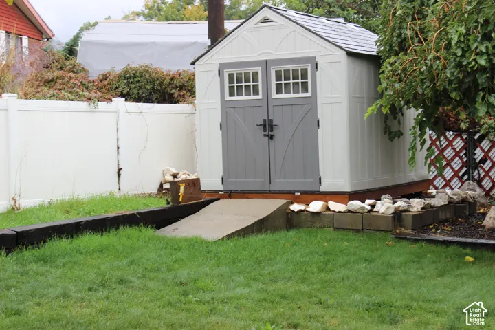 Storage shed featuring double-door entry with windows, composite exterior, and a dedicated concrete access ramp, enclosed by perimeter vinyl fencing