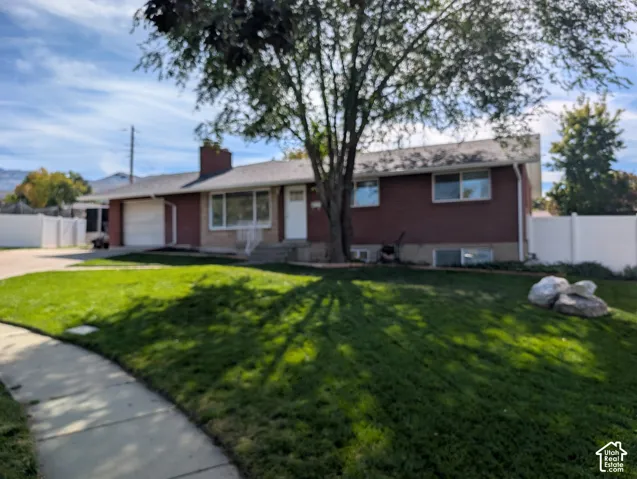 Red brick exterior, attached garage, concrete driveway, mature front yard tree, and front sidewalk