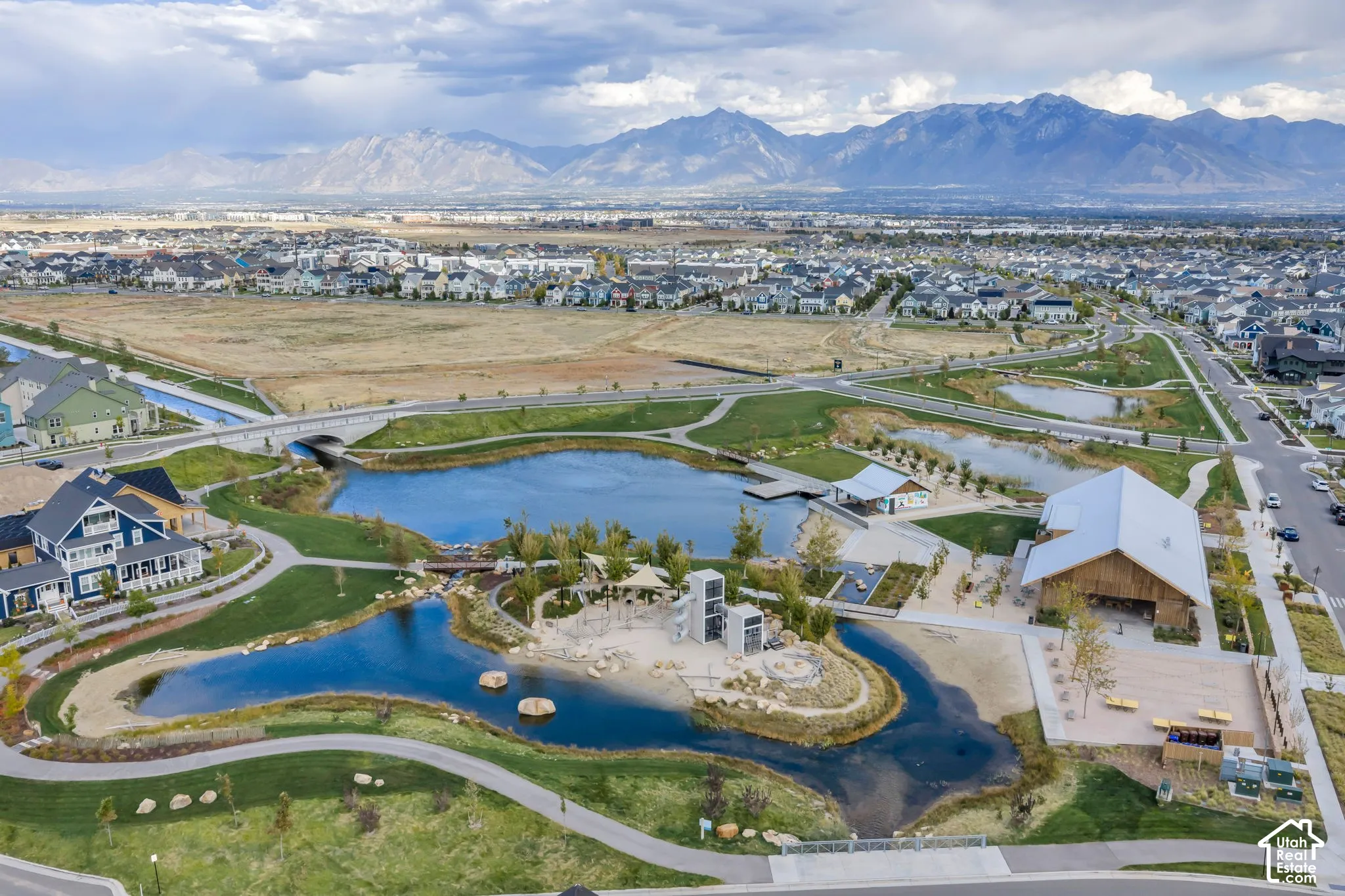 Aerial perspective featuring community ponds, paved walking paths, landscaped green spaces, a central sandy beach area, and mountain backdrop
