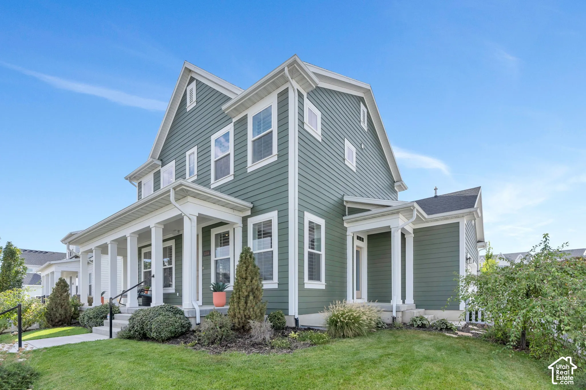 Two-story exterior featuring sage green horizontal lap siding, a covered front porch with classic columns, crisp white trim, and a gabled roofline