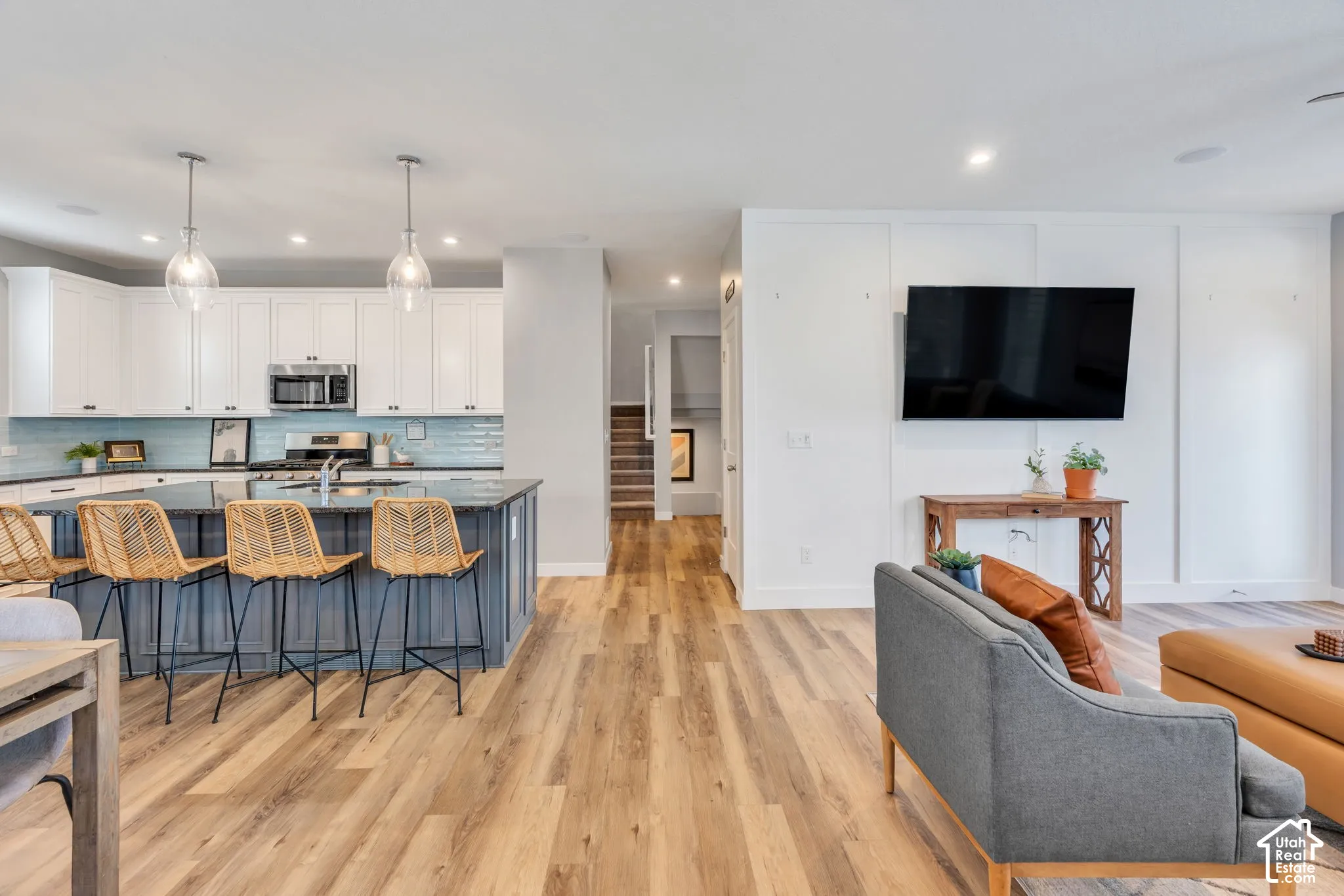 Kitchen featuring white cabinetry, a center island with contrasting base, wood-finish flooring, glass pendant lighting, and wall board-and-batten detailing