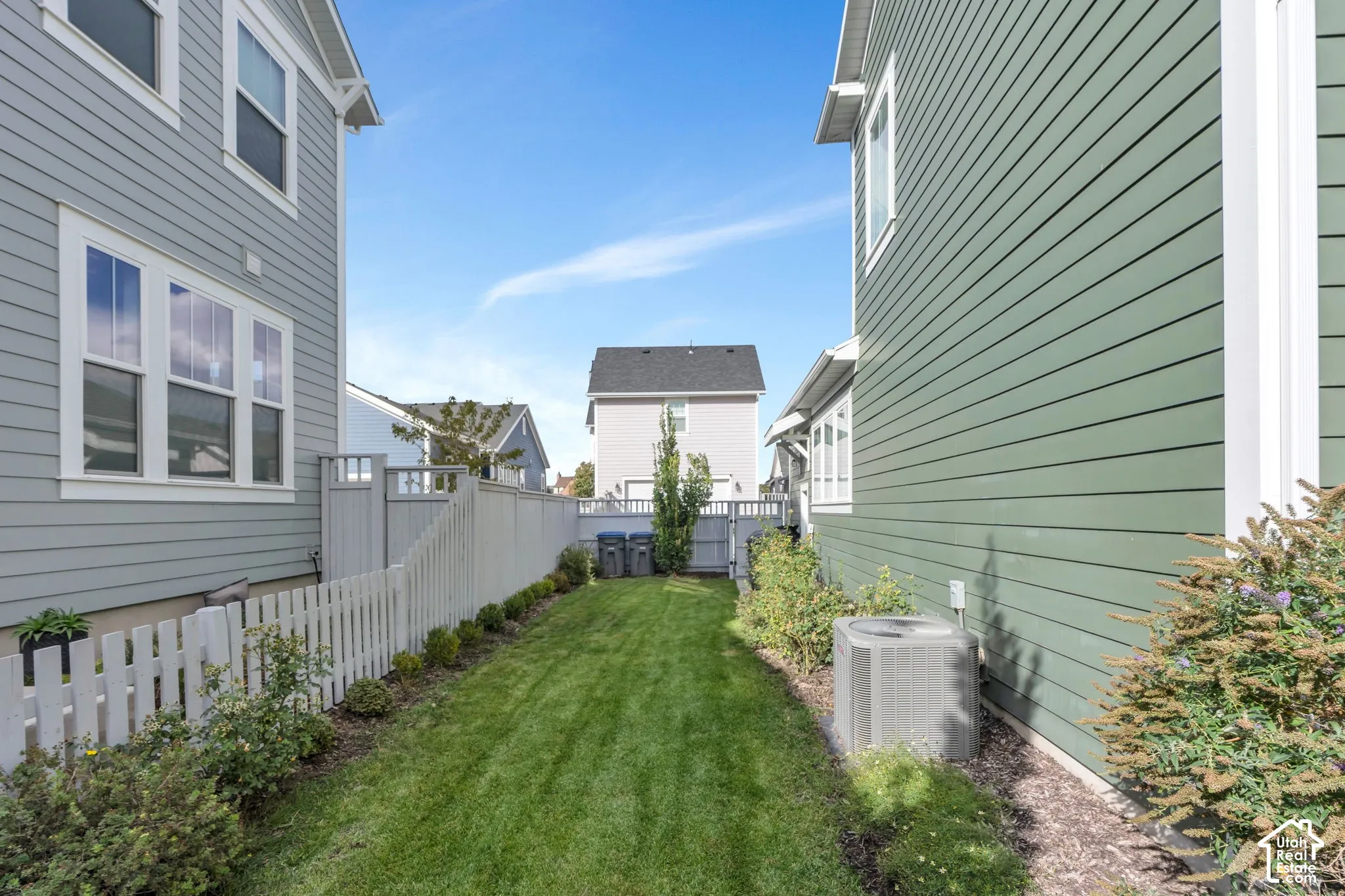 Exterior side yard featuring horizontal lap siding, a white picket fence, manicured grass lawn, and low-maintenance landscaping