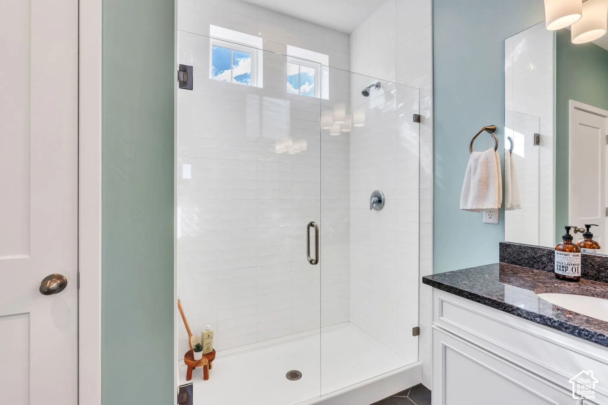 Walk-in shower featuring a frameless glass enclosure, white subway-style wall tile, a built-in recessed light, and a high-contrast dark stone vanity countertop