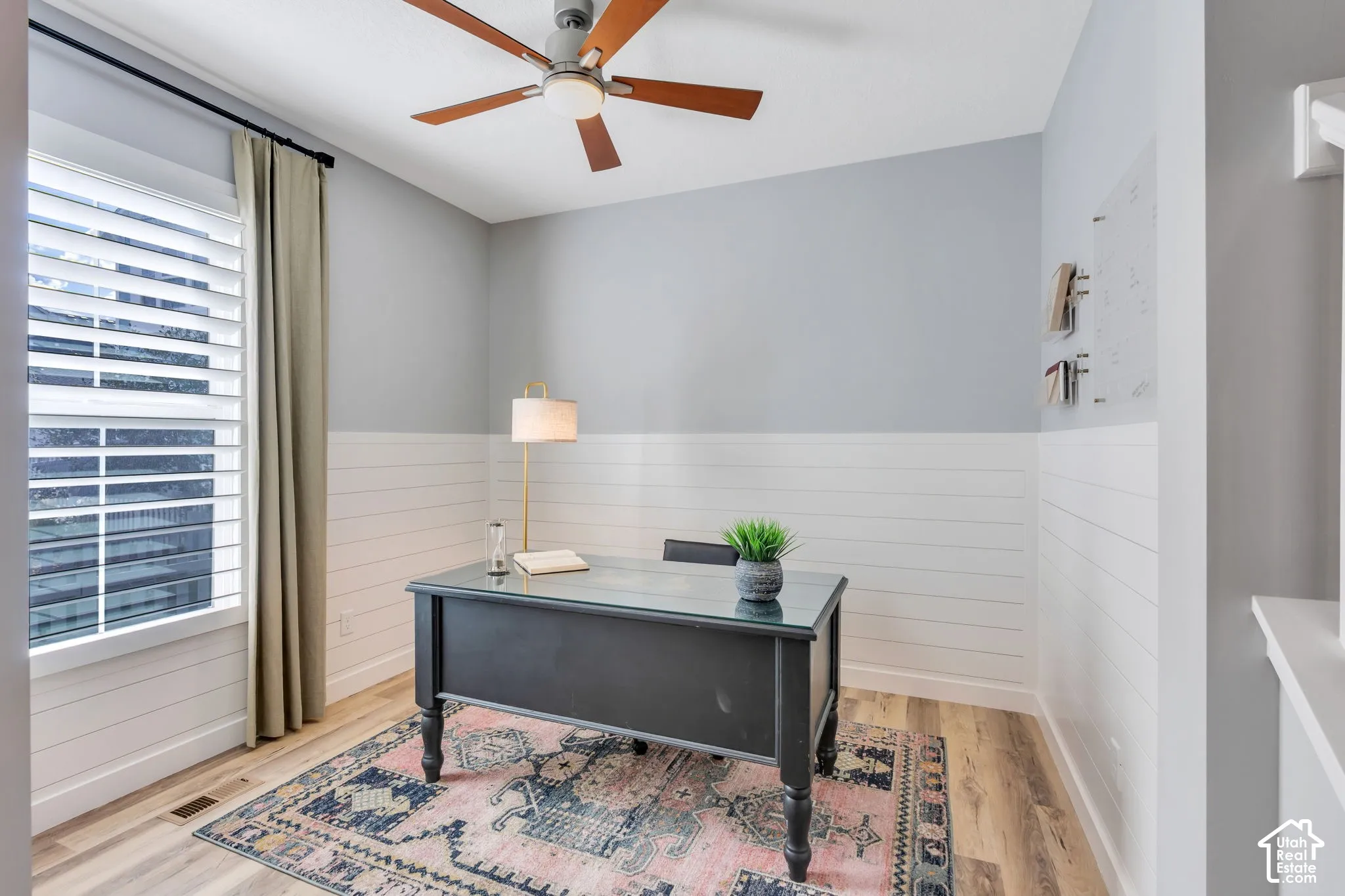 Room featuring horizontal shiplap wall paneling, wood-finish flooring, a window with plantation shutters, and a ceiling fan with integrated lighting