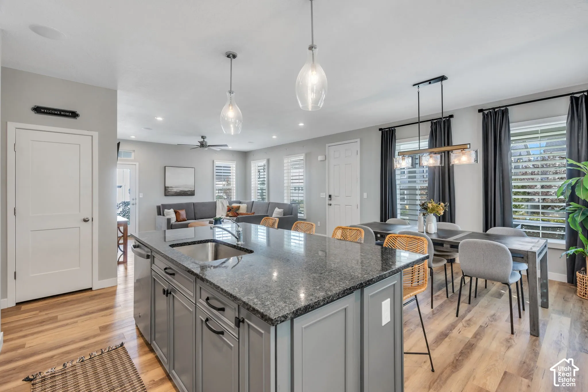 Kitchen island featuring a stone countertop, under-mount stainless steel sink, and shaker-style cabinetry, complemented by wood-finish flooring and pendant lighting