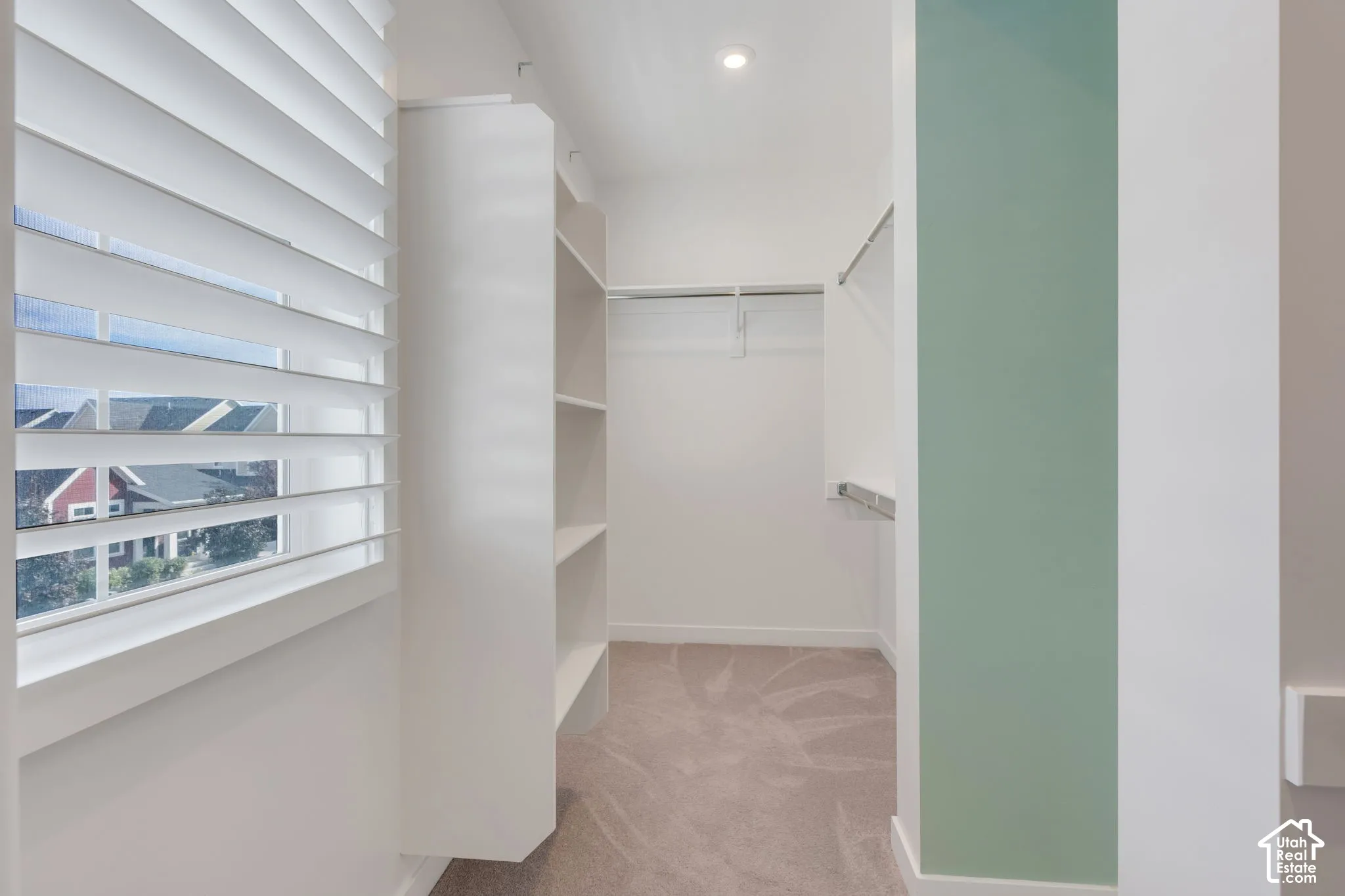 Walk-in closet featuring white built-in shelving, adjustable horizontal window blinds, wall-to-wall carpeting, and metal hanging rods