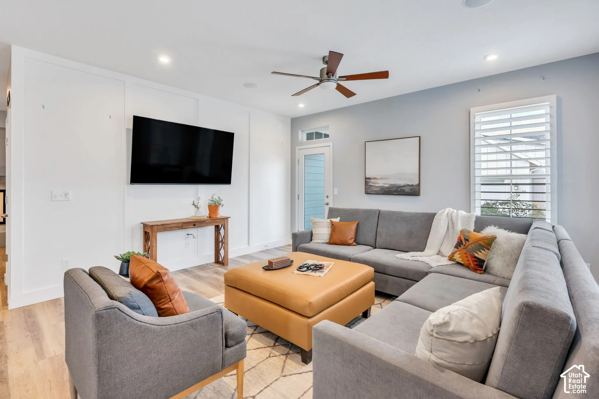 Living area featuring vertical wall paneling, wood-finish flooring, recessed lighting, ceiling fan, and plantation shutter window treatments