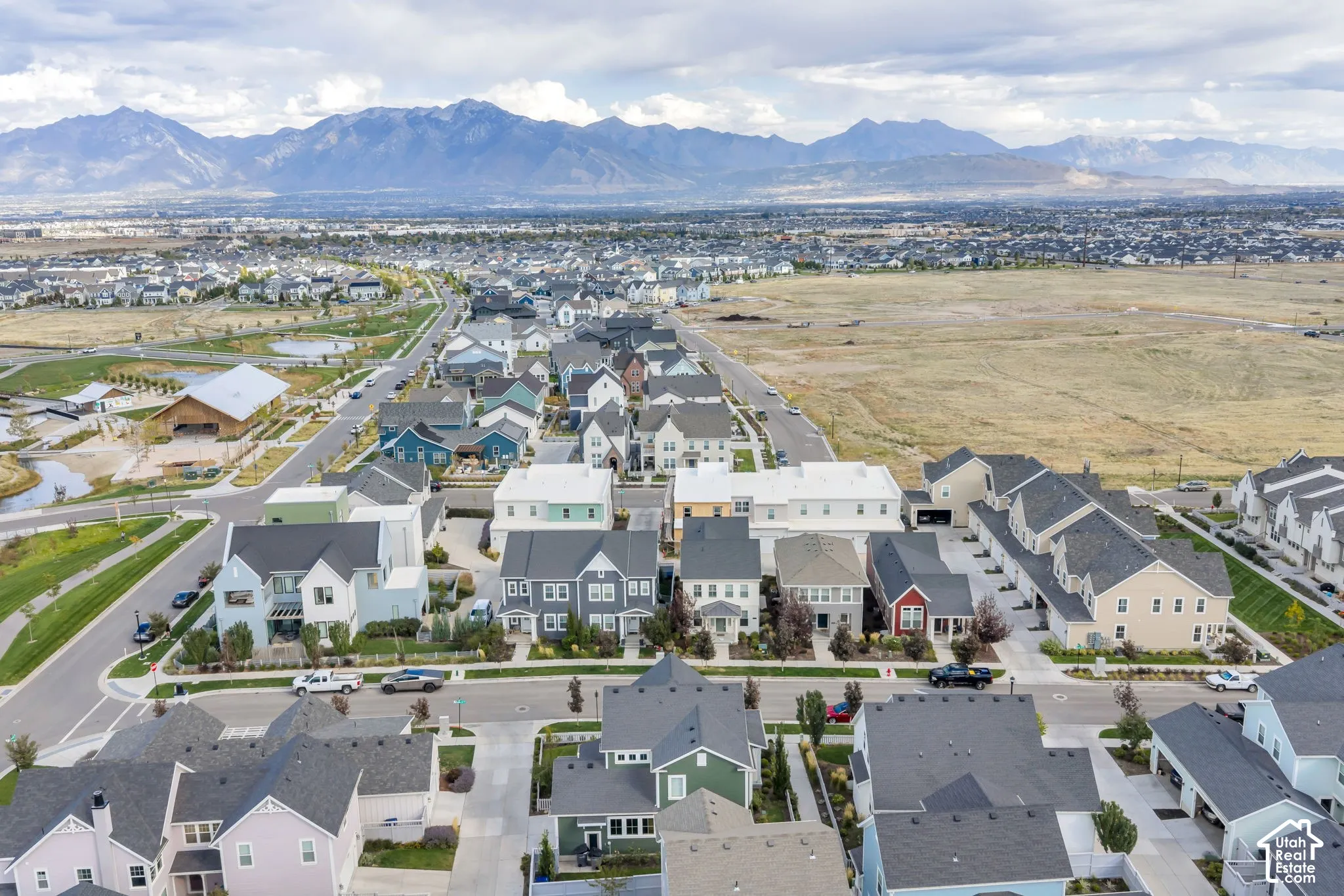 Aerial perspective of a planned community featuring multi-story residential architecture, paved thoroughfares, manicured landscaping, and mountain backdrops