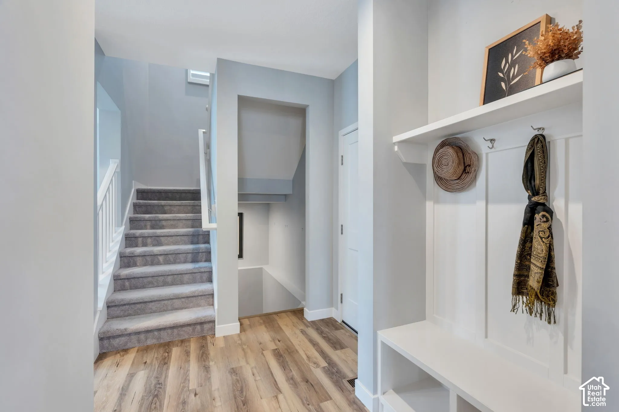 Entryway featuring wood-finish flooring, built-in mudroom bench with shelving, wainscot wall paneling, and staircase with carpeted treads