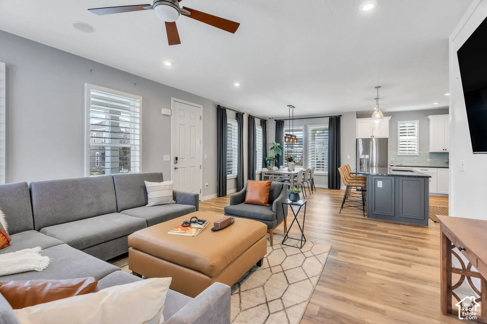 Open-concept living space featuring wood-finish flooring, recessed lighting, a ceiling fan, and a center kitchen island with dark cabinetry