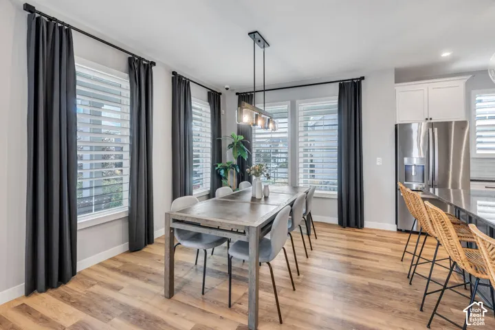 Open-concept dining area featuring wood-finish flooring, large windows with plantation shutters, and a modern industrial pendant light fixture