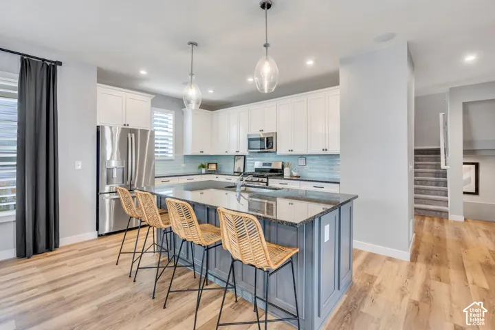 Kitchen featuring white shaker-style cabinetry, dark-tone stone countertops, stainless steel appliances, a center island with contrasting cabinetry, and wood-finish flooring