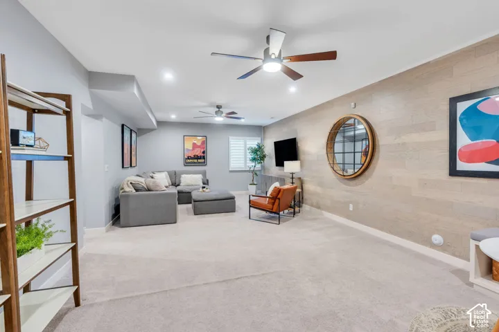 Open-concept living space featuring wood-plank accent wall, recessed lighting, dual ceiling fans, and neutral wall-to-wall carpeting