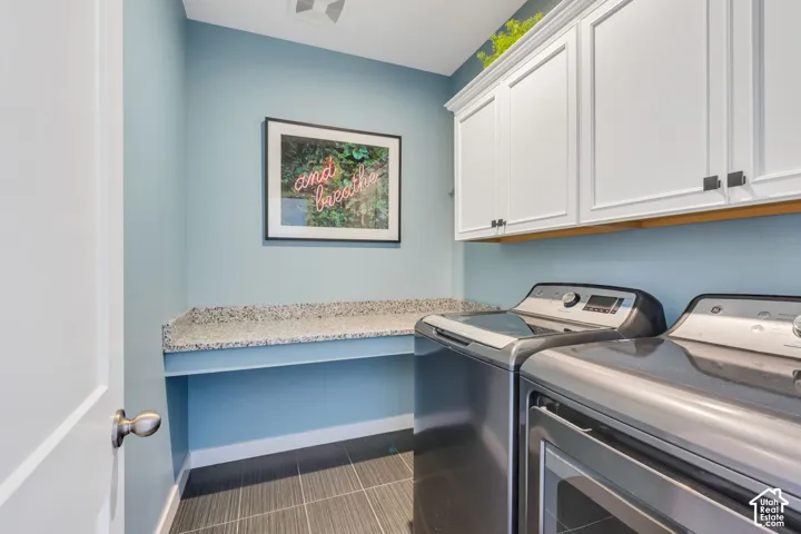 Laundry area featuring white shaker-style wall cabinetry, integrated stone-finish countertop, and dark-toned tile flooring