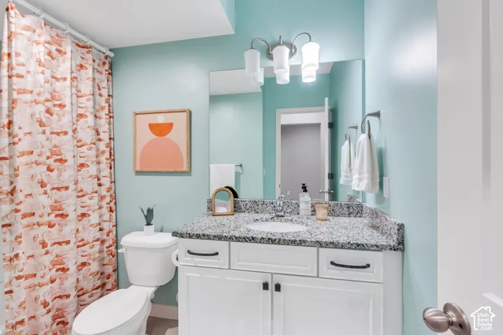 Bathroom featuring a white vanity cabinet with stone-finish countertop, undermount sink, multi-bulb vanity light fixture, and large frameless mirror