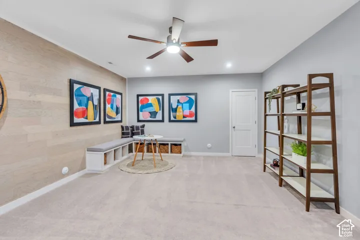 Interior space featuring a light wood-tone wall accent, built-in storage bench with shelving, neutral carpeting, recessed ceiling lighting, and a multi-blade ceiling fan