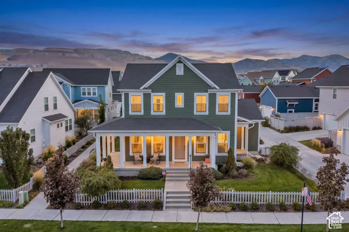 Two-story residence featuring horizontal lap siding, an expansive covered front porch with columns, a picket fence, and mountain scenery