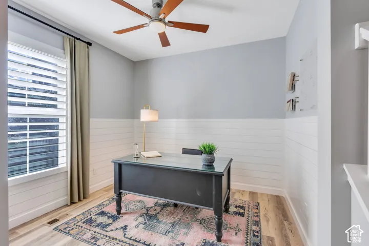Room featuring horizontal shiplap wall paneling, wood-finish flooring, a window with plantation shutters, and a ceiling fan with integrated lighting