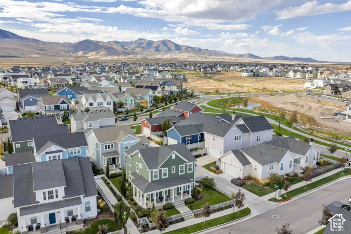 Aerial perspective of a multi-level residence featuring a covered front porch, an attached two-car garage, white picket fencing, and prominent mountain backdrops