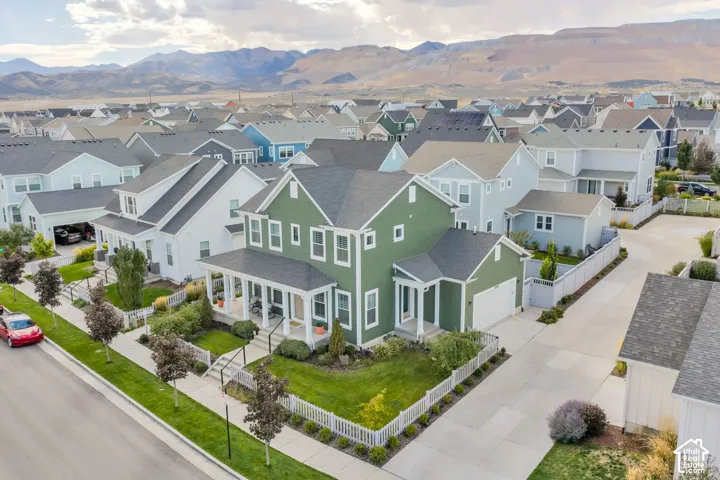 Two-story residence featuring a covered front porch, white picket fencing, attached garage, and mountain backdrop