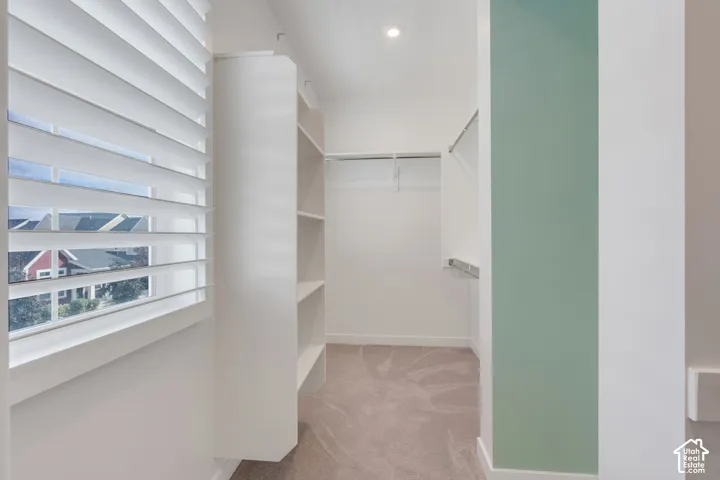 Walk-in closet featuring white built-in shelving, adjustable horizontal window blinds, wall-to-wall carpeting, and metal hanging rods