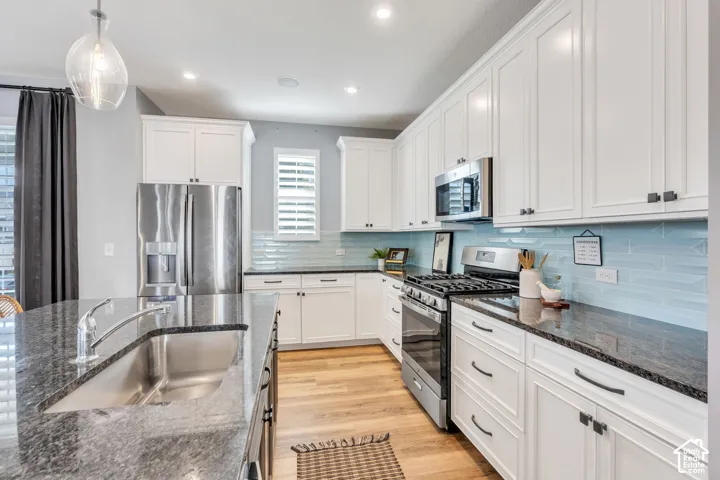 Kitchen featuring white shaker-style cabinetry, stone countertops, stainless steel appliances, a tile backsplash, and wood-finish flooring