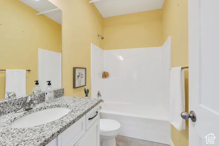 Bathroom featuring white cabinetry, stone-finish countertop with an integrated basin, wall-mounted mirror, and a tub-shower combination with a surround finish