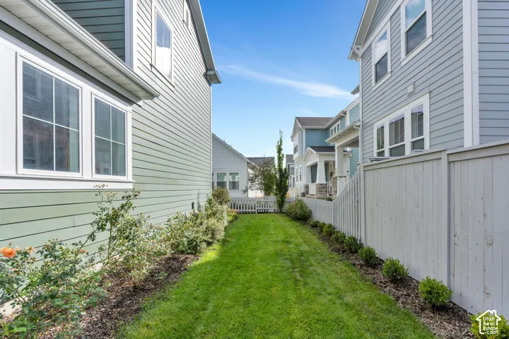 Side yard featuring horizontal lap siding, manicured lawn, established shrubbery, and a wood privacy fence