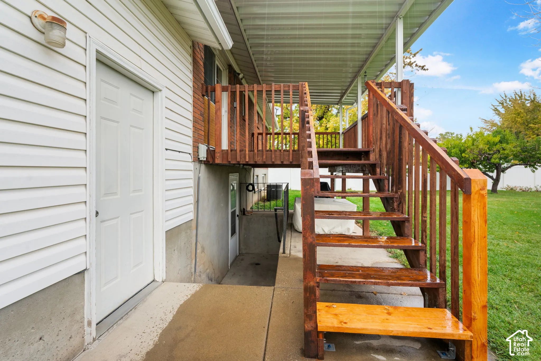 Exterior staircase with stained wood finish and railings, elevated deck with overhead covering, concrete lower-level walkout entrance, and horizontal siding
