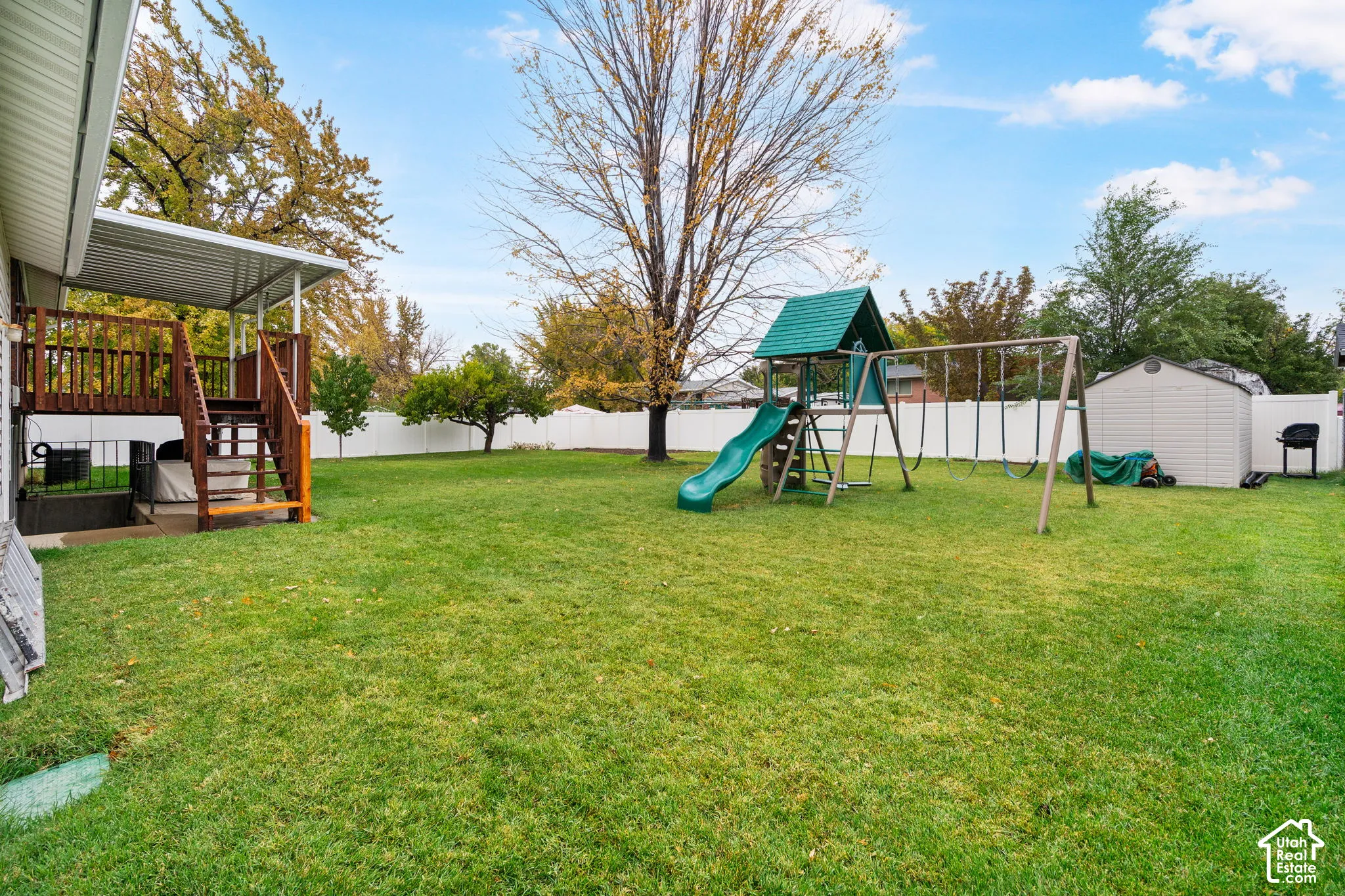Fenced backyard featuring an elevated wooden deck with a covered patio, a detached storage shed, and mature trees