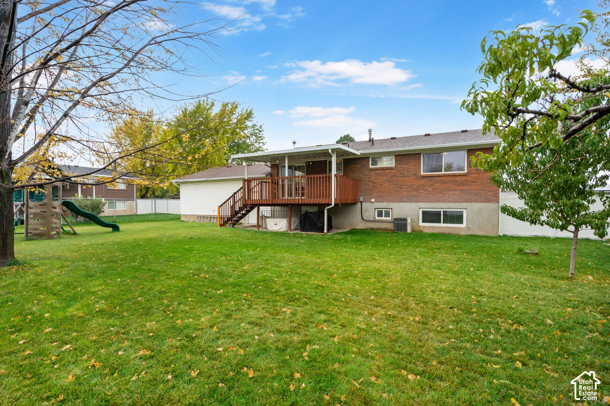 Expansive backyard featuring a large grass lawn, mature trees, and a wooden deck with railing