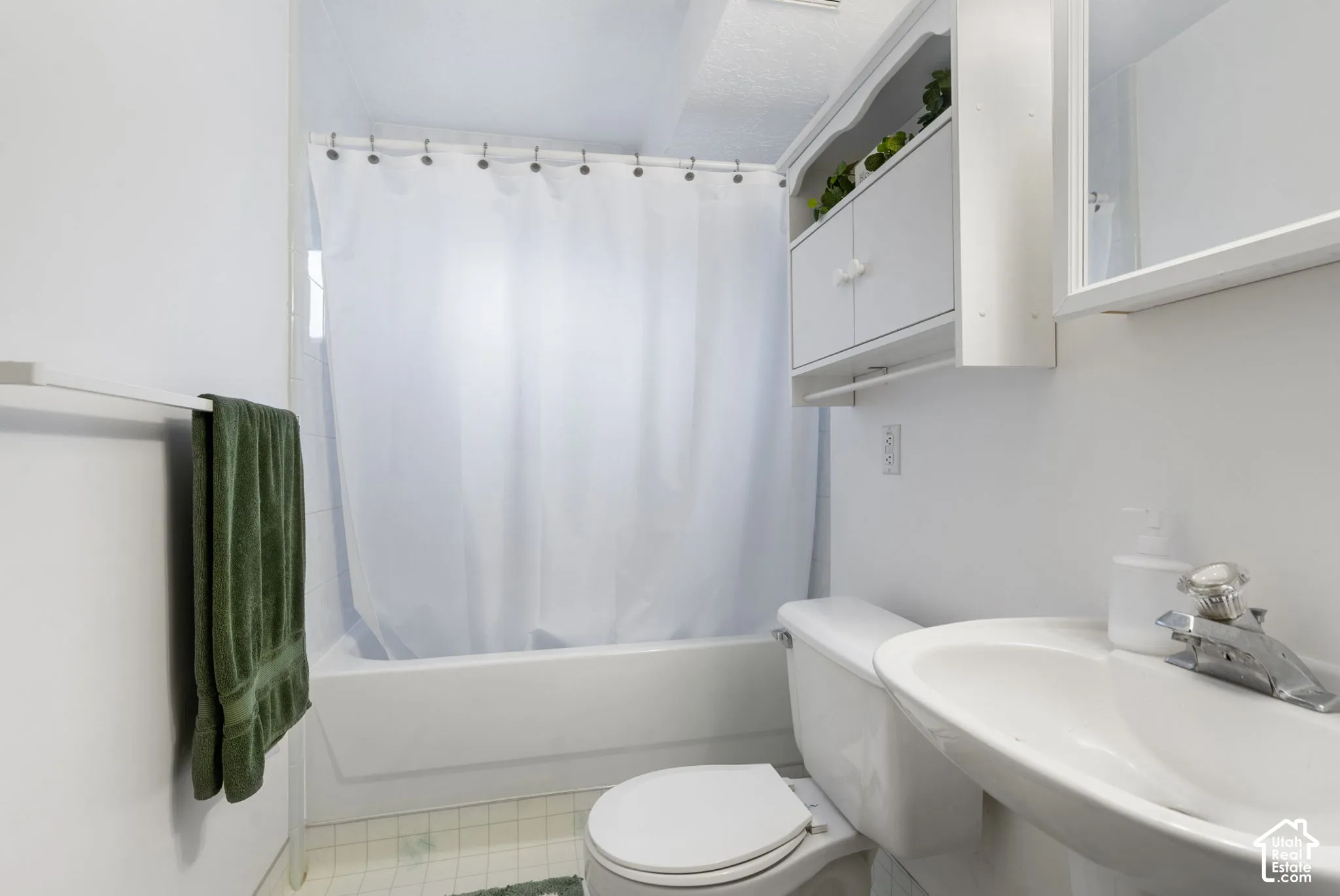 Full bathtub with tile surround, pedestal sink, chrome hardware, and white built-in wall cabinetry