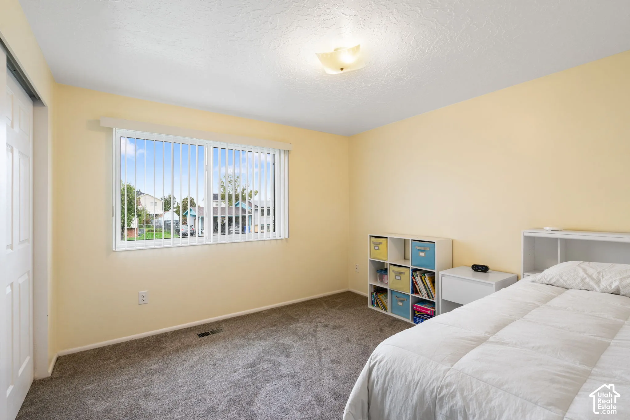 Room featuring neutral wall tones, carpeted flooring, a sliding-door closet, a single-pane window with vertical blinds, and a flush-mount ceiling light